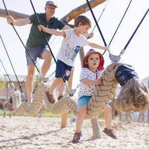 Vater und zwei Kinder turnen auf einem Kletterseil auf einem Spielplatz